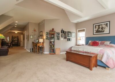 A spacious bedroom with a blue headboard, tan carpet, and an adjoining hallway.