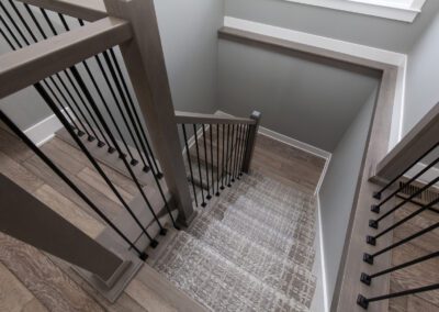 Modern staircase with wooden steps, metal balusters, and a gray patterned carpet runner.