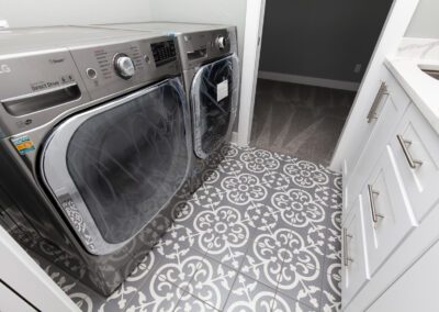 Modern laundry room with front-load washer and dryer, white cabinetry, and decorative patterned tile flooring.