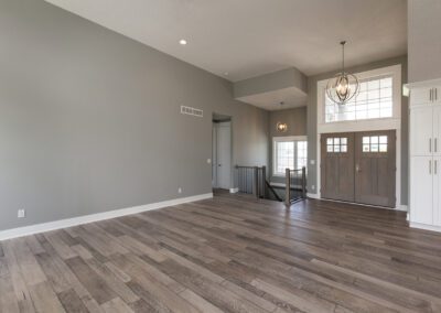 An empty room with gray walls, hardwood floors, and a chandelier above the entrance area.