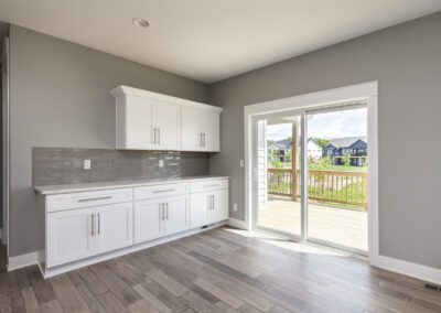 Modern kitchen interior with white cabinetry and gray backsplash, leading out to a wooden deck through sliding glass doors.