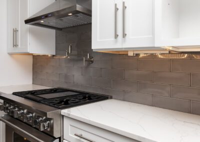 Modern kitchen with stainless steel stove, white cabinets, and gray backsplash.