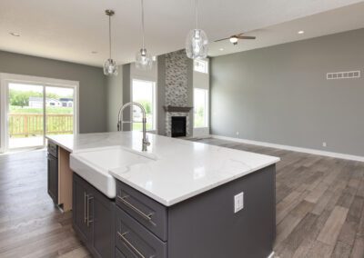 Modern kitchen with a marble countertop island, stainless steel appliances, and pendant lighting, overlooking a spacious living area with a fireplace.