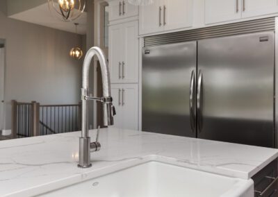 Modern kitchen interior featuring a stainless steel refrigerator and a farmhouse sink with a high-arc faucet.