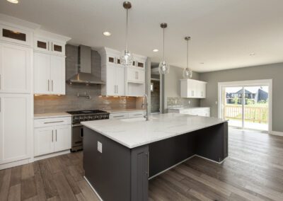 Modern kitchen interior with white cabinetry, dark island, stainless steel appliances, and pendant lighting.