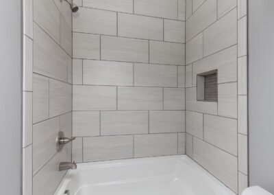 A modern bathroom corner with tiled walls and a built-in bathtub.