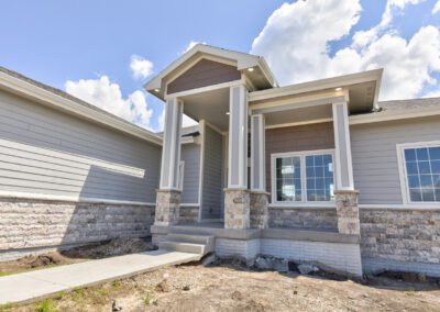 New suburban house featuring a covered porch with stone columns and a clear blue sky with clouds in the background.